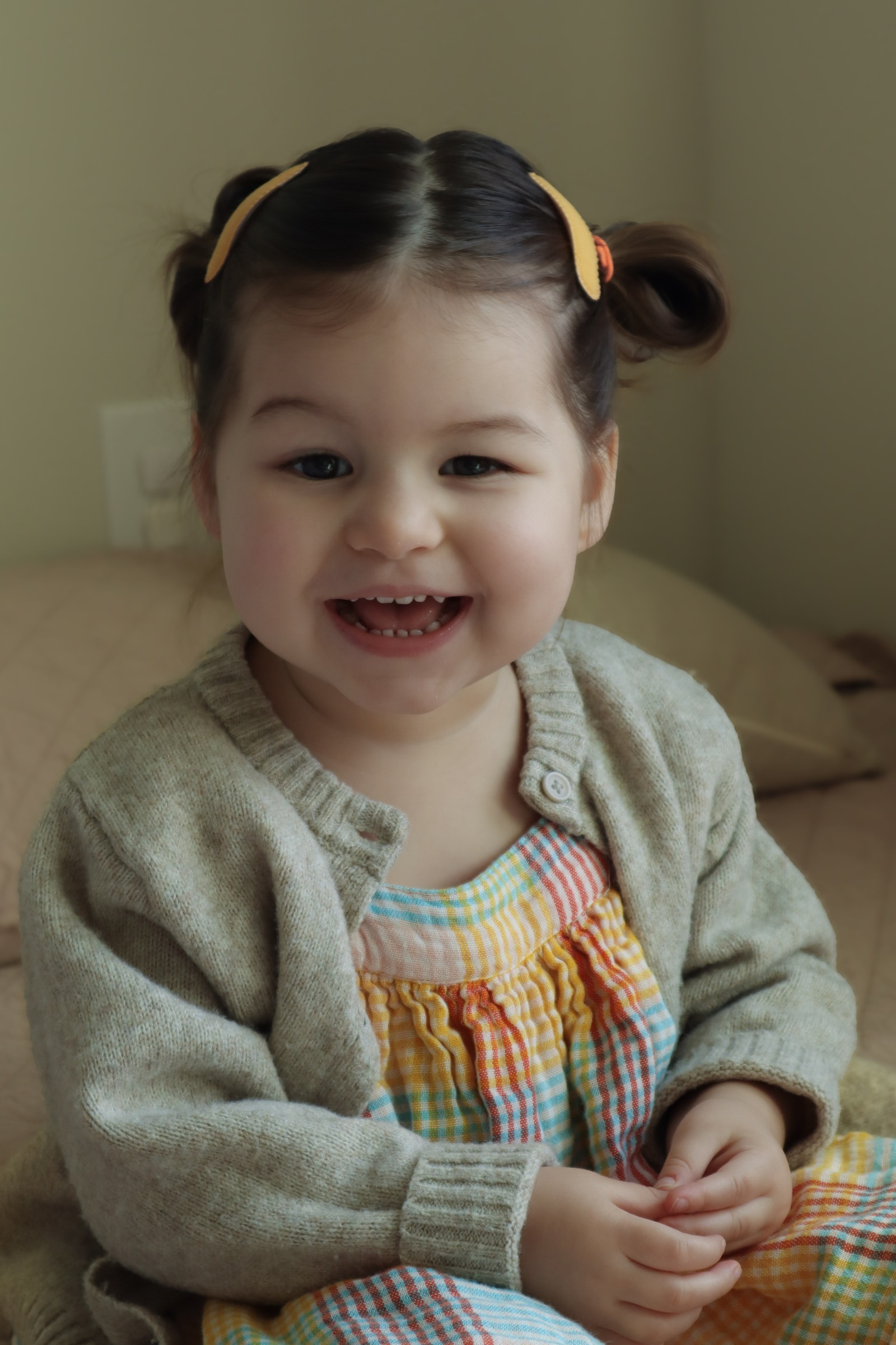 A baby girl in a knit cardigan smiling brightly
