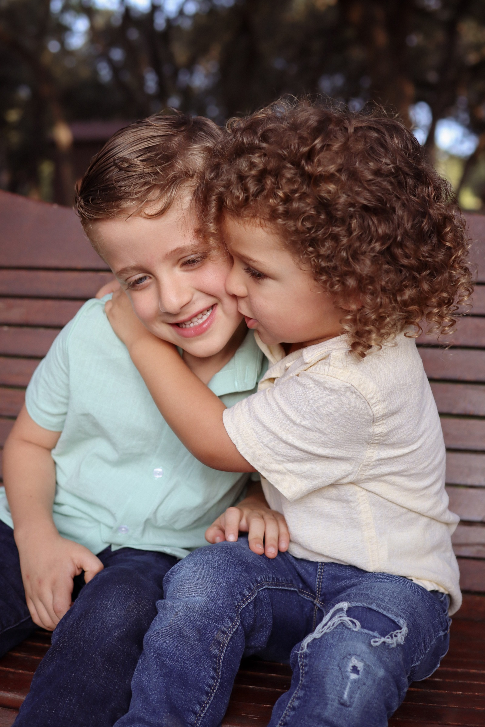 Two young brothers on a bench, one kissing the other on the cheek