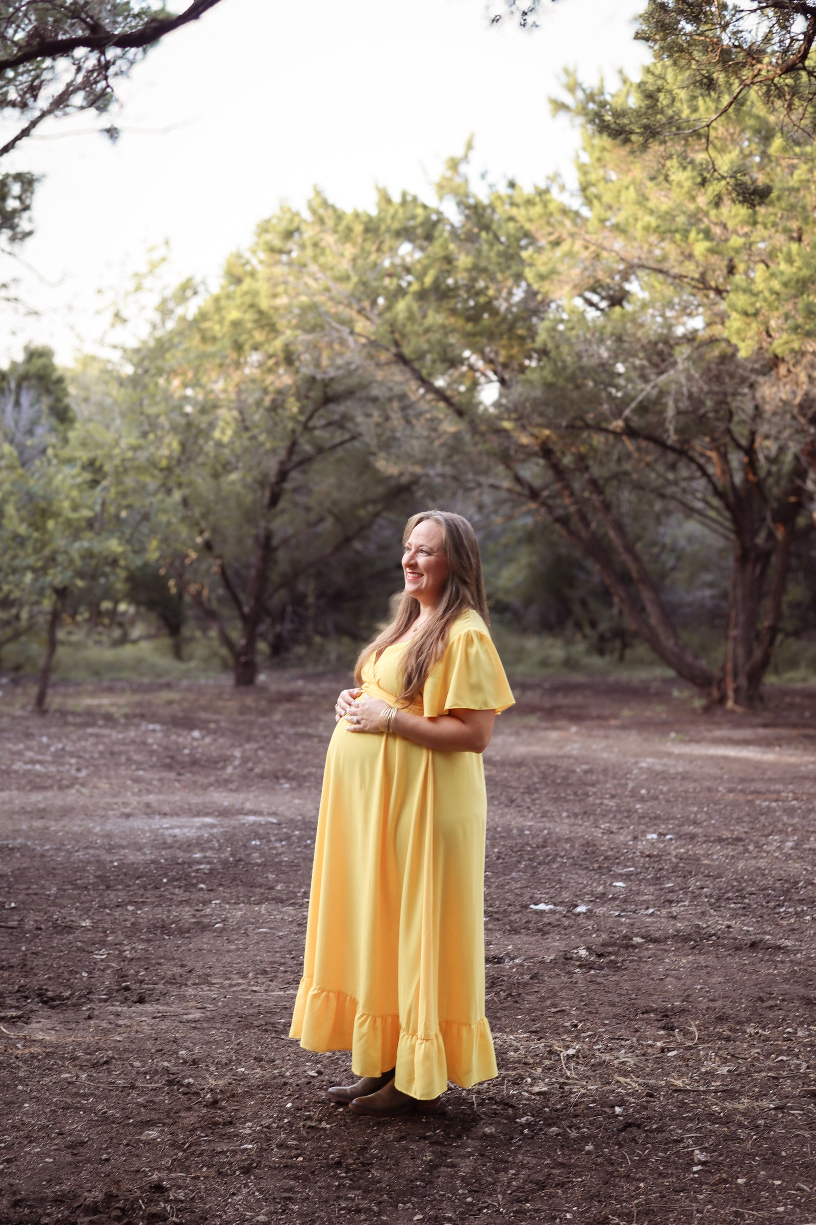 Expectant mother in a yellow dress laughing among the trees