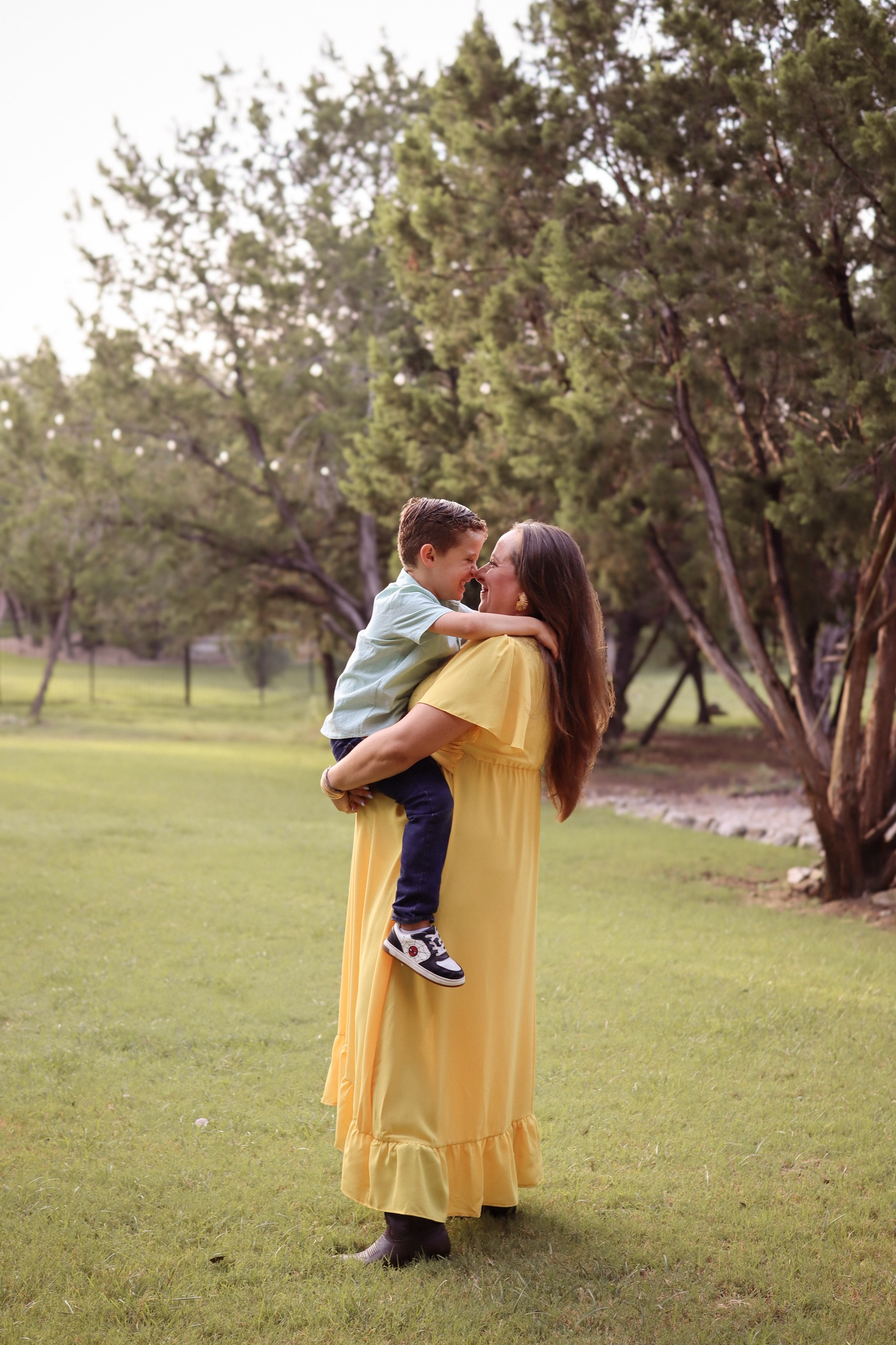 A mother lifting her son into her arms, foreheads touching, in a green Texas field
