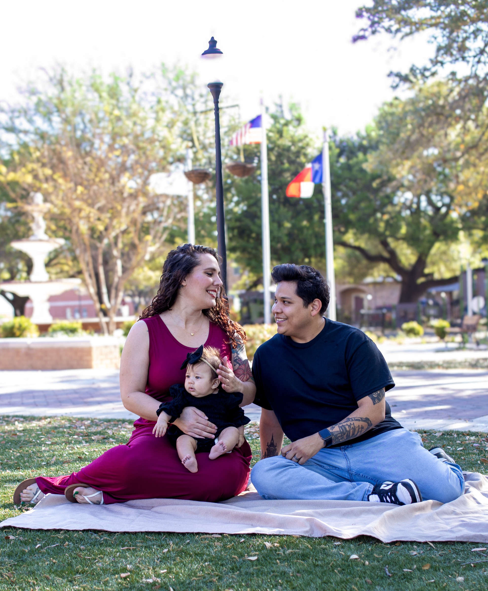 A couple sitting on a blanket in a park with their baby