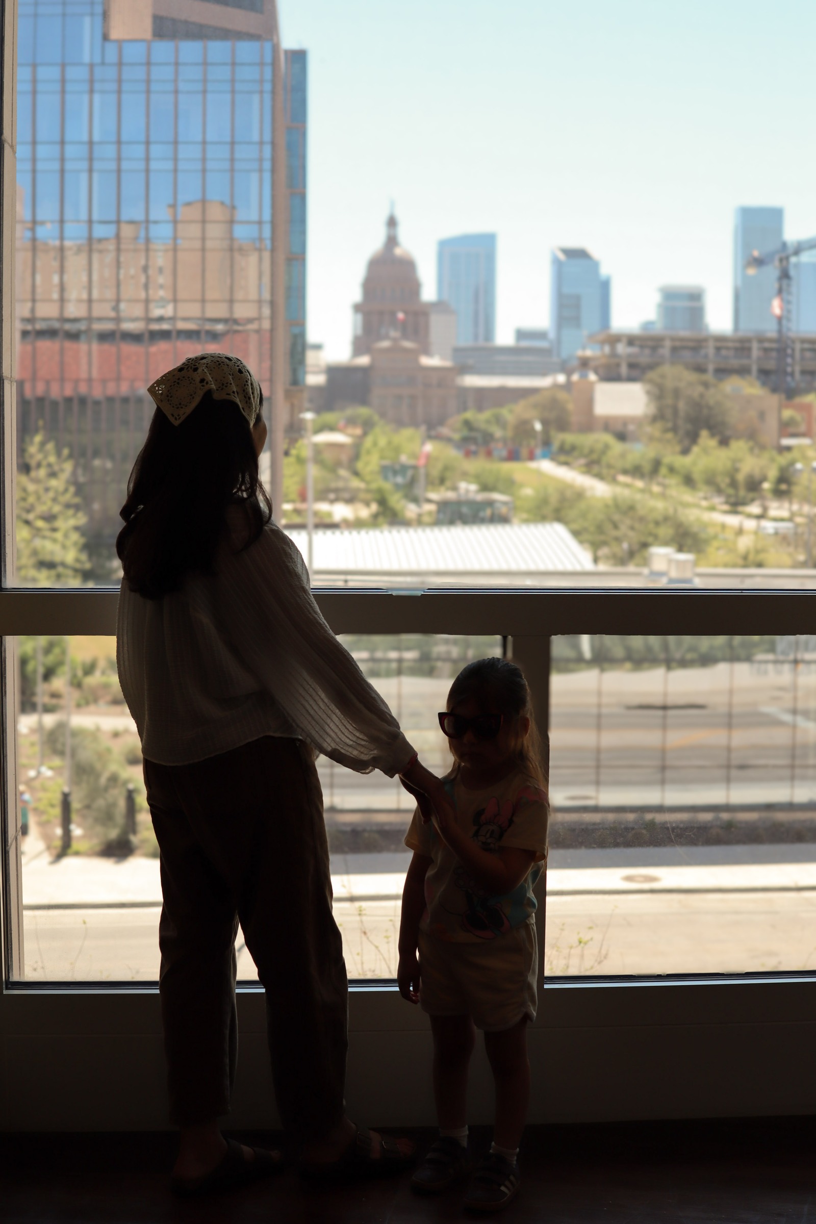 A mother and daughter silhouetted against a window overlooking the Austin skyline